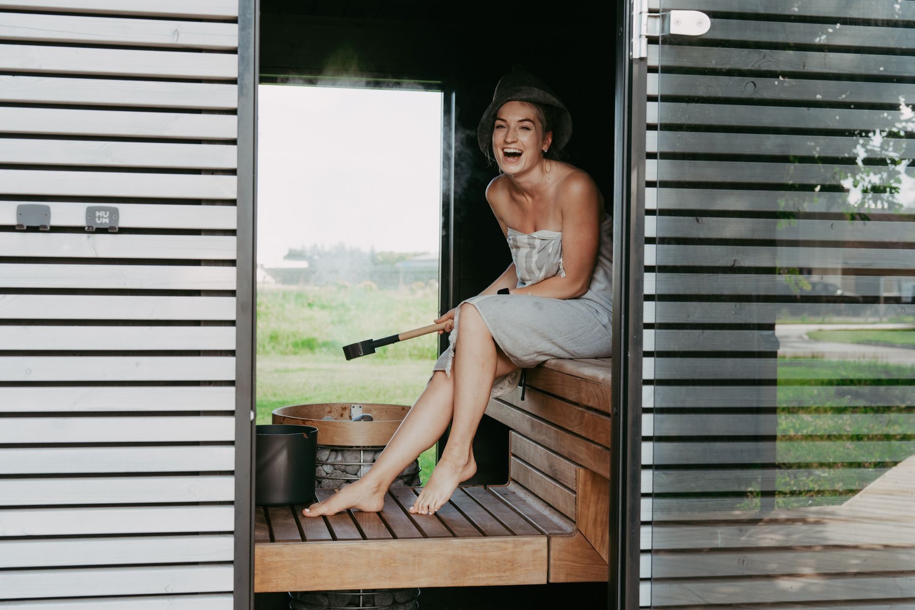 A woman in a felt sauna hat laughing in a sauna doorway